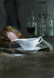 Pillivuyt Sauceboat with Handle on a wooden table, filled with pan sauce. Accompanied by a partially carved roast, carving knife, and a green napkin.