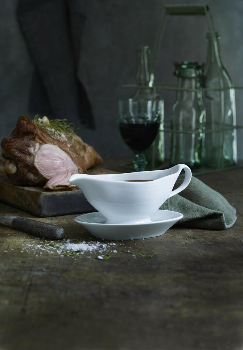Pillivuyt Sauceboat with Handle on a wooden table, filled with pan sauce. Accompanied by a partially carved roast, carving knife, and a green napkin.