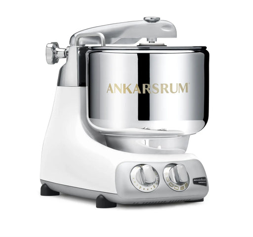 Ankarsrum Assistent Original stand mixer with polished stainless-steel bowl on a white base, featuring control knobs for speed and timer settings.