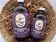My Elderberry Fairy | Elderberry Syrup - 16 oz, featuring two bottles in a basket, showcases organic ingredients for versatile use in drinks and recipes.