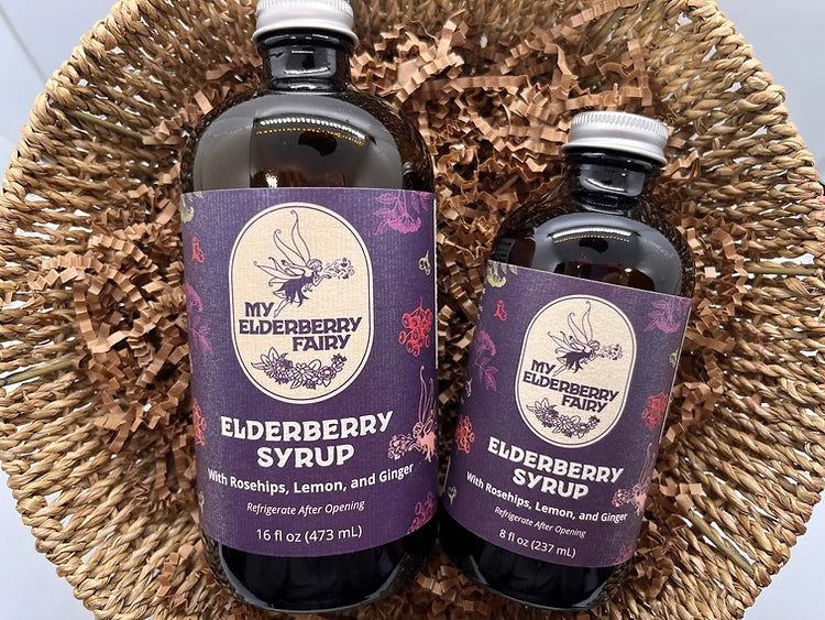 My Elderberry Fairy | Elderberry Syrup - 16 oz, featuring two bottles in a basket, showcases organic ingredients for versatile use in drinks and recipes.