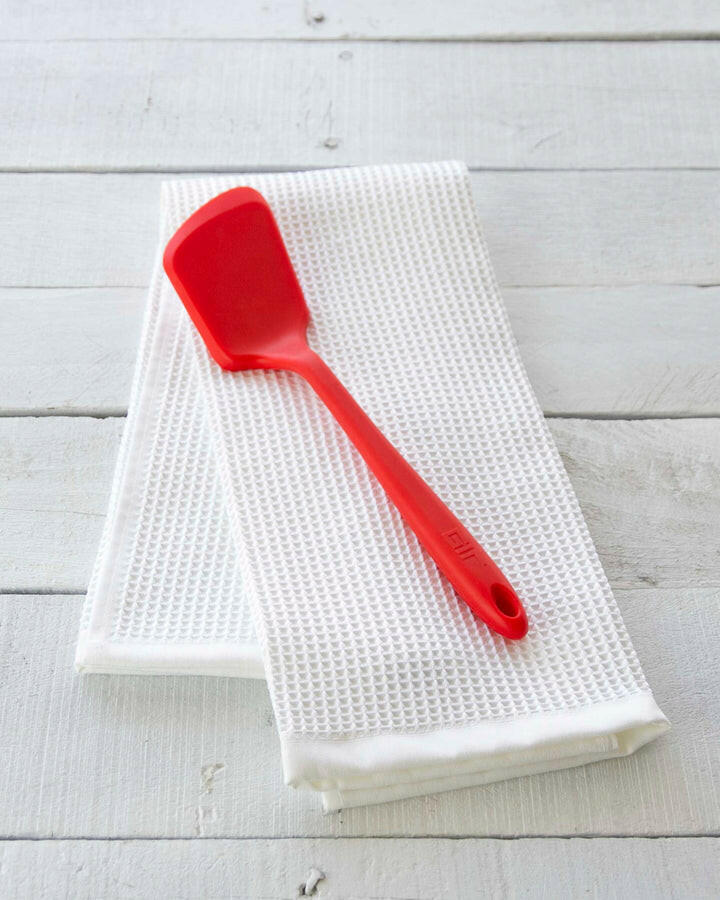 GIR | Ultimate Flip - Teal, a spatula designed for delicate dishes, rests on a towel, showcasing its sturdy yet flexible construction for non-stick cookware.