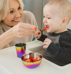 A woman feeds a baby using the Ahimsa Stainless Steel Kids Dishes - Fork + Spoon Set, promoting healthy eating with durable, safe, and engaging toddler utensils.