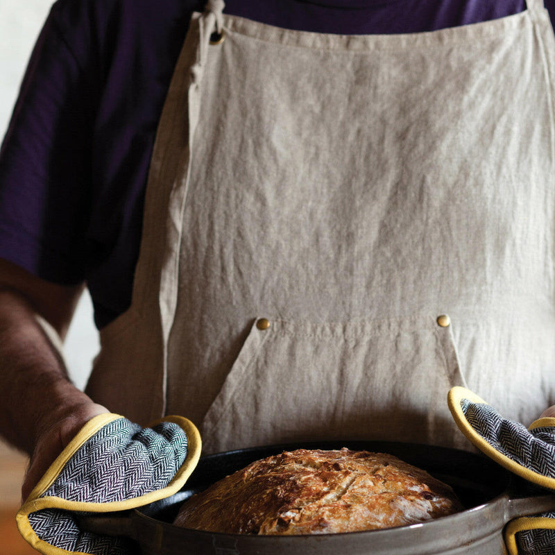 Person in apron holds loaf, showcasing Sir|Madam | Linen Grand Apron - Faded Black, highlighting apron’s comfort and practicality with waist compartments and adjustable neck loop.