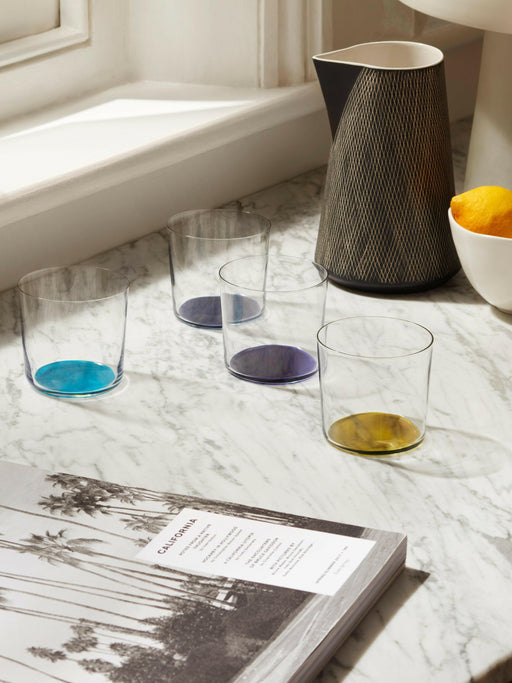 LSA International Coro Tumblers on a marble surface, featuring four clear glasses with colored bases, alongside a black carafe and lemons in a white bowl.
