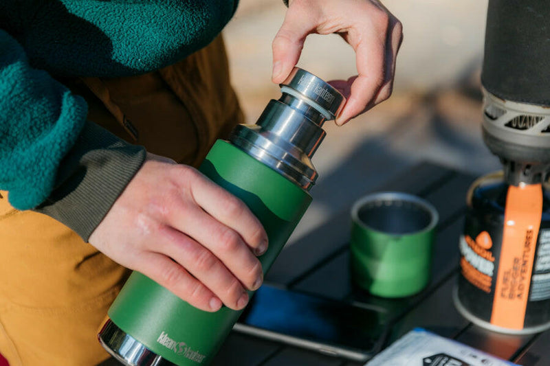 Person holding Klean Kanteen 25oz Insulated Thermos with Built-In Cup and Pourer, showcasing its versatile, plastic-free design for outdoor and urban adventures.