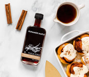 Runamok Maple Syrups - Smoked with Pecan Wood, showcased with tableware, highlighting its infusion of maple, cinnamon, and vanilla, ideal for breakfast or desserts.