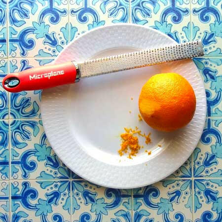 Microplane | Premium Zester, Grater - Classic Blue with grated orange zest on a white plate, showcasing its precision on a blue-and-white patterned surface.