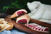 Spotted Trotter | Sliced Charcuterie Meats - Duck Prosciutto displayed on a wooden surface, accompanied by crackers, showcasing its marinated, thin-sliced presentation.