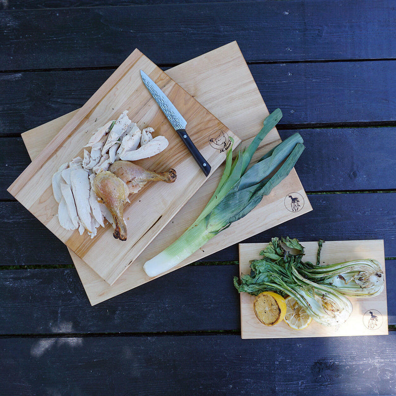 J.K. Adams | Maple Reversible Prep Boards - 16 x 12 showcasing meal prep versatility with carved poultry, grilled greens, and a whole leek on a dark wooden surface.