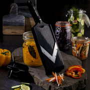 Microplane Adjustable V-Blade Mandoline Slicer amid sliced vegetables and pickled jars, showcasing its precise cutting ability for meal prep.
