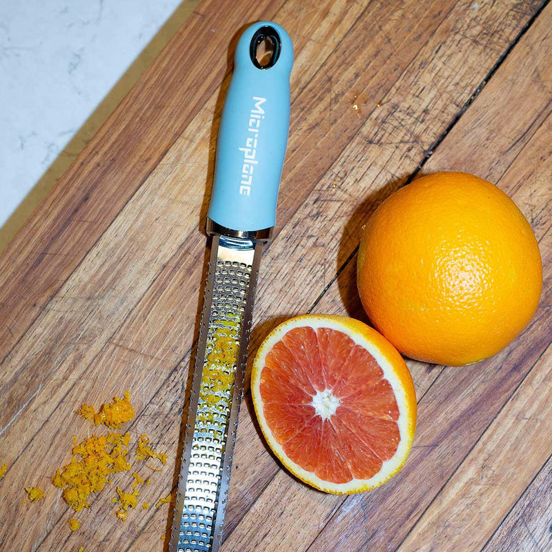 Microplane | Premium Zester, Grater - Classic Blue on a wooden board with an orange, showcasing its precision zesting capabilities with freshly grated zest alongside.